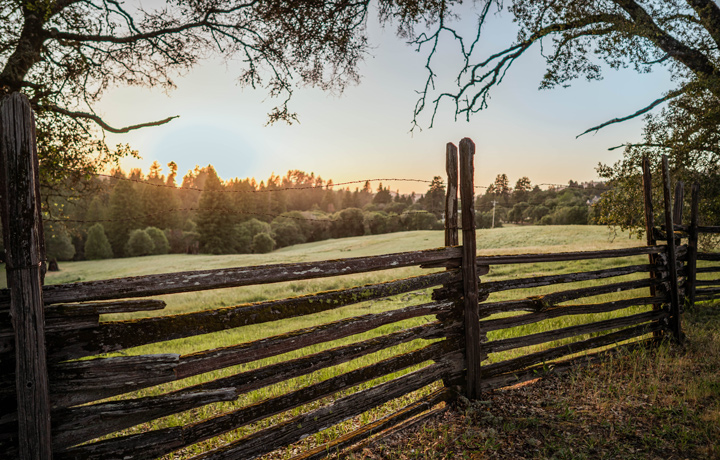 The sun sets behind a split rail fence